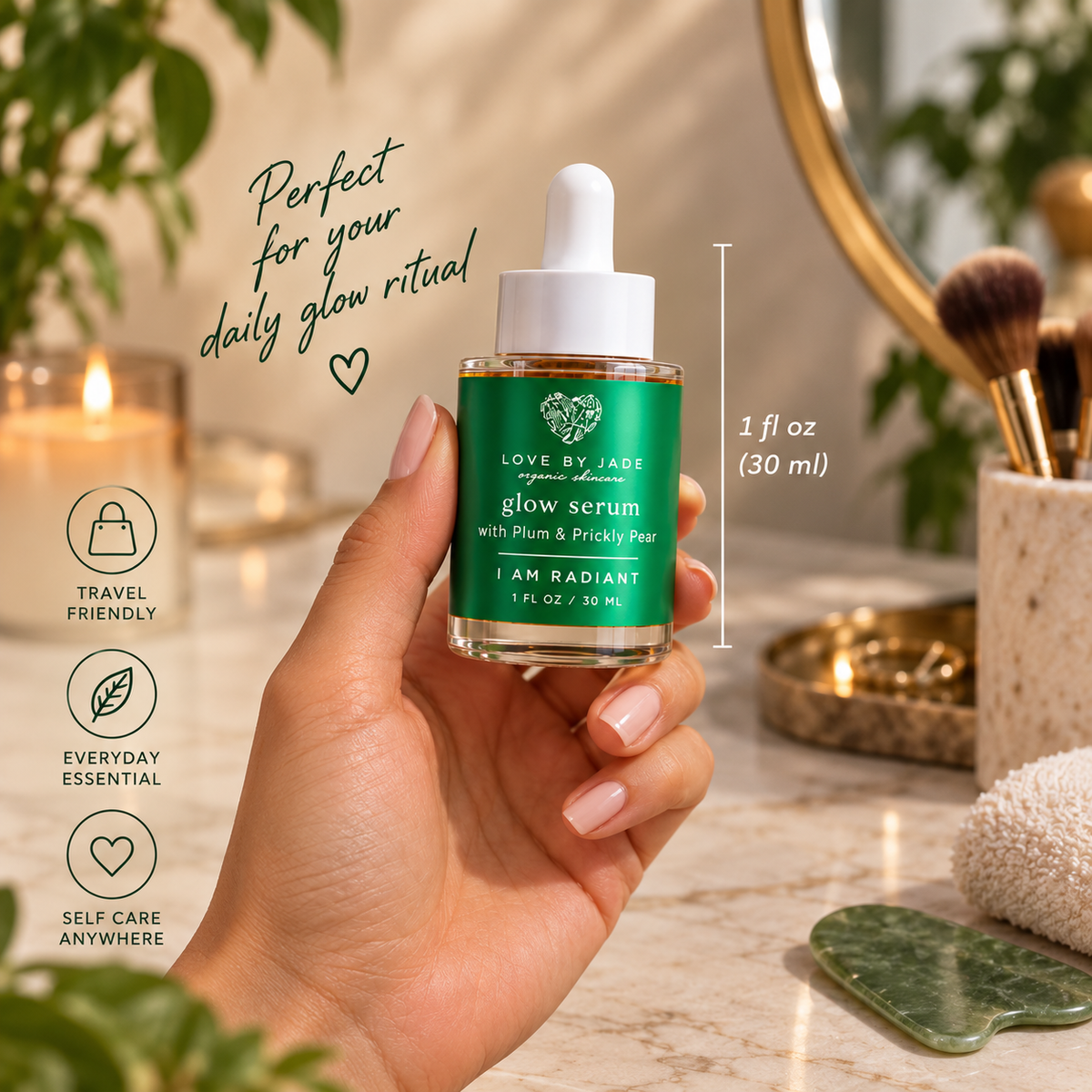 A hand holds a small glass dropper bottle of Love by Jade Glow Serum with a green label and white dropper cap. The scene is a softly lit vanity setup with candles, makeup brushes, a mirror, and spa-like props in the background.